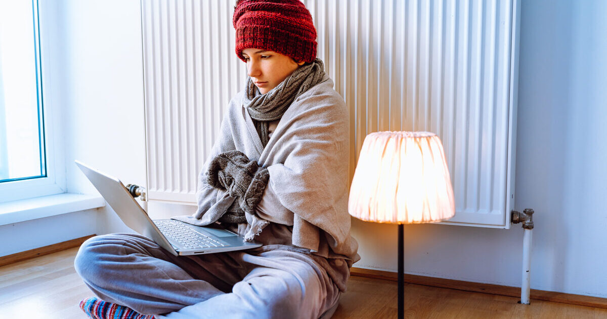 young woman bundled up beside heater