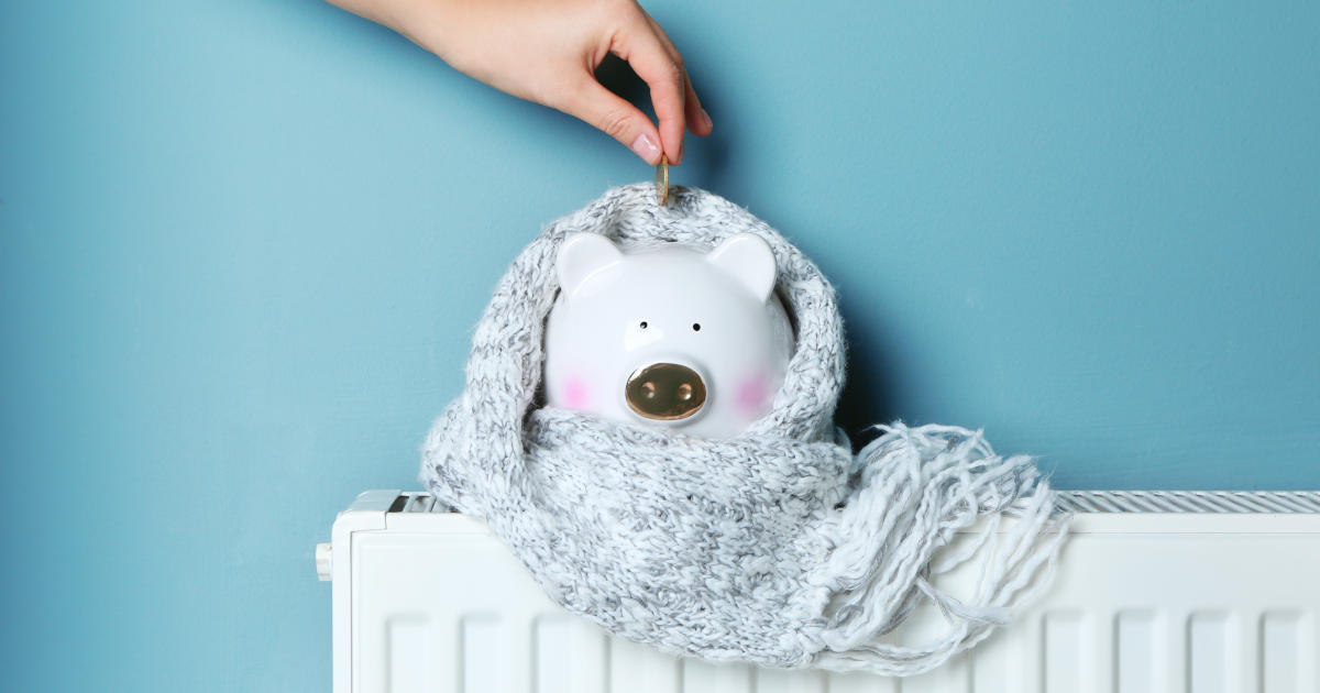 hand dropping coin in piggy bank on heater